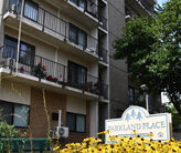 Exterior of a tall brick-and-concrete apartment building with a sign that reads, 'Parkland Place' and a patch of yellow flowers.