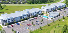 Aerial view of two 3-story buildings with a pool and a low-rise building centered in the parking lot.