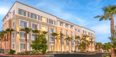 A four-story building with a stucco exterior in a desert environment, lined with palm trees.