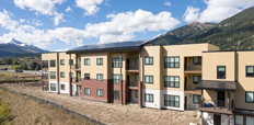 Exterior photograph of three-story apartment building with mountains in the background.