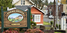 The welcome sign of Boring, Oregon, with houses and other buildings in the background.