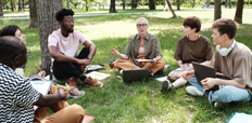 A group of young adults sitting in a circle in a grassy park.