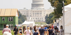 A crowd of people at the National Mall in Washington, D.C., with exhibits lined up on the right and a model house on the left. The United States Capitol can be seen in the background.
