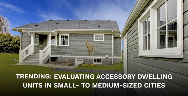 A grey house on a green lawn and a matching detached garage.
