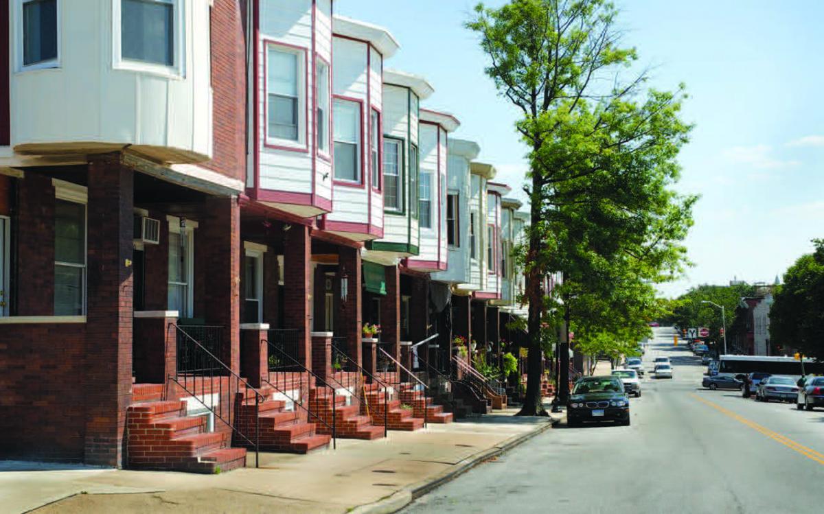 Angled view of two-story rowhomes fronting a street with parked cars.