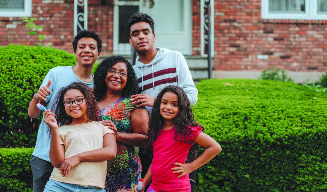 A woman standing surrounded by four kids in front of a home.