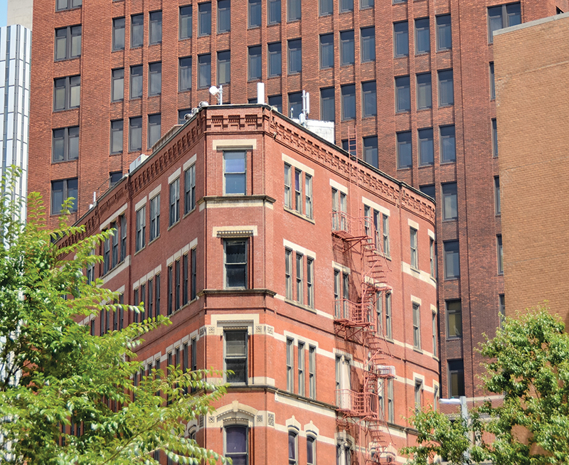 Partial view of a triangular multistory building in front of another taller building.