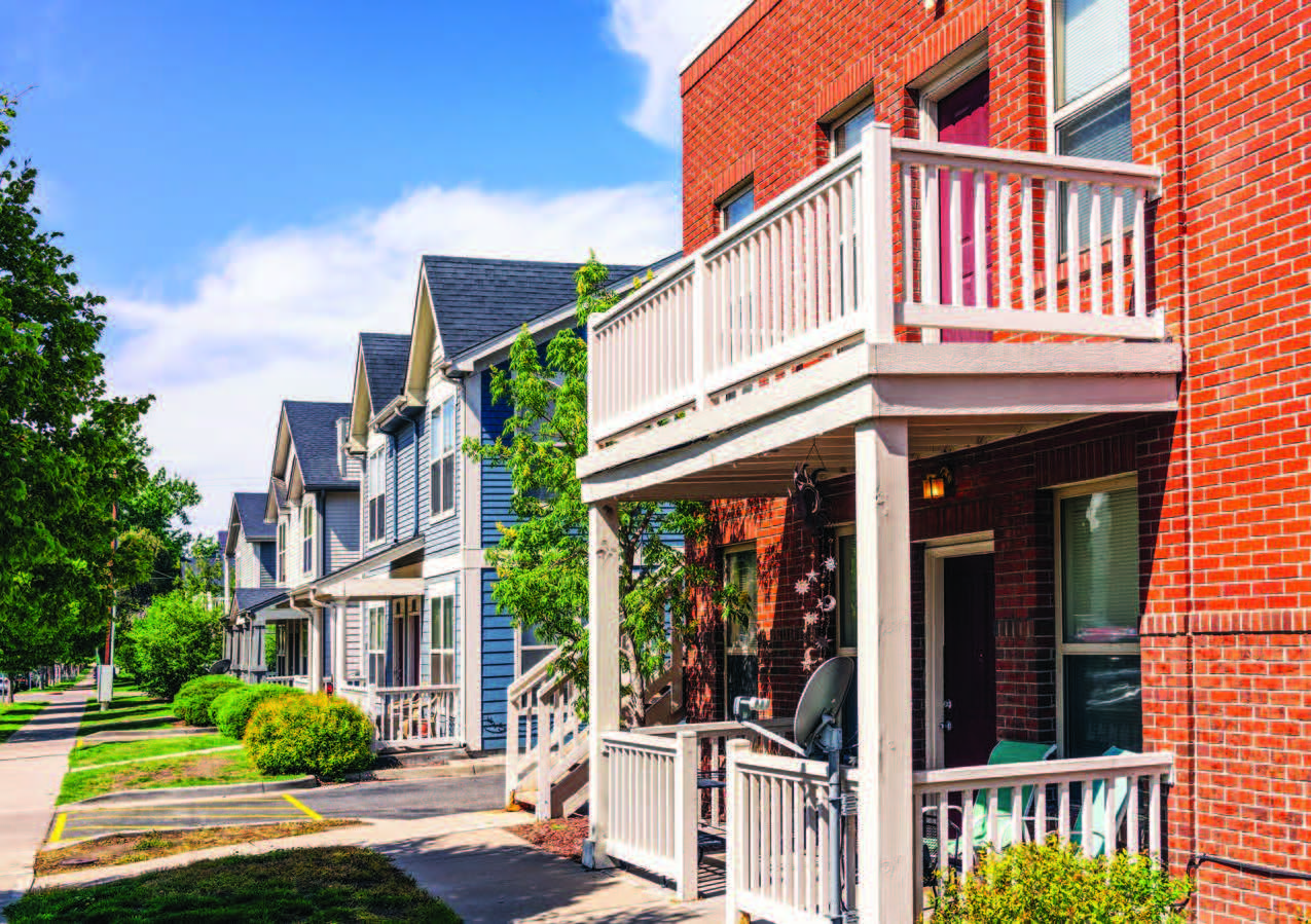 An angled-view of a row of two-story homes with sidewalk and trees.