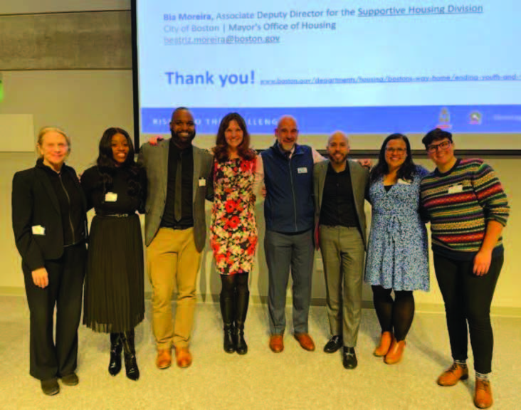 A group of people standing in front of a projection screen with text on it.