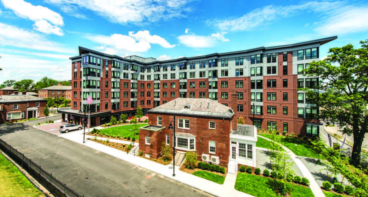 Two sides of a six-story building with a smaller two-story building in the foreground and lawn in between.