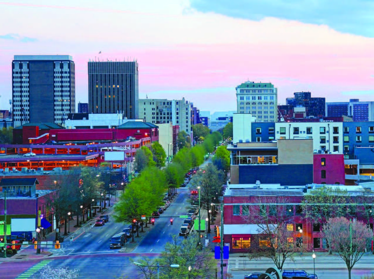 A four-lane roadway with trees in the median and buildings of various sizes on either side.