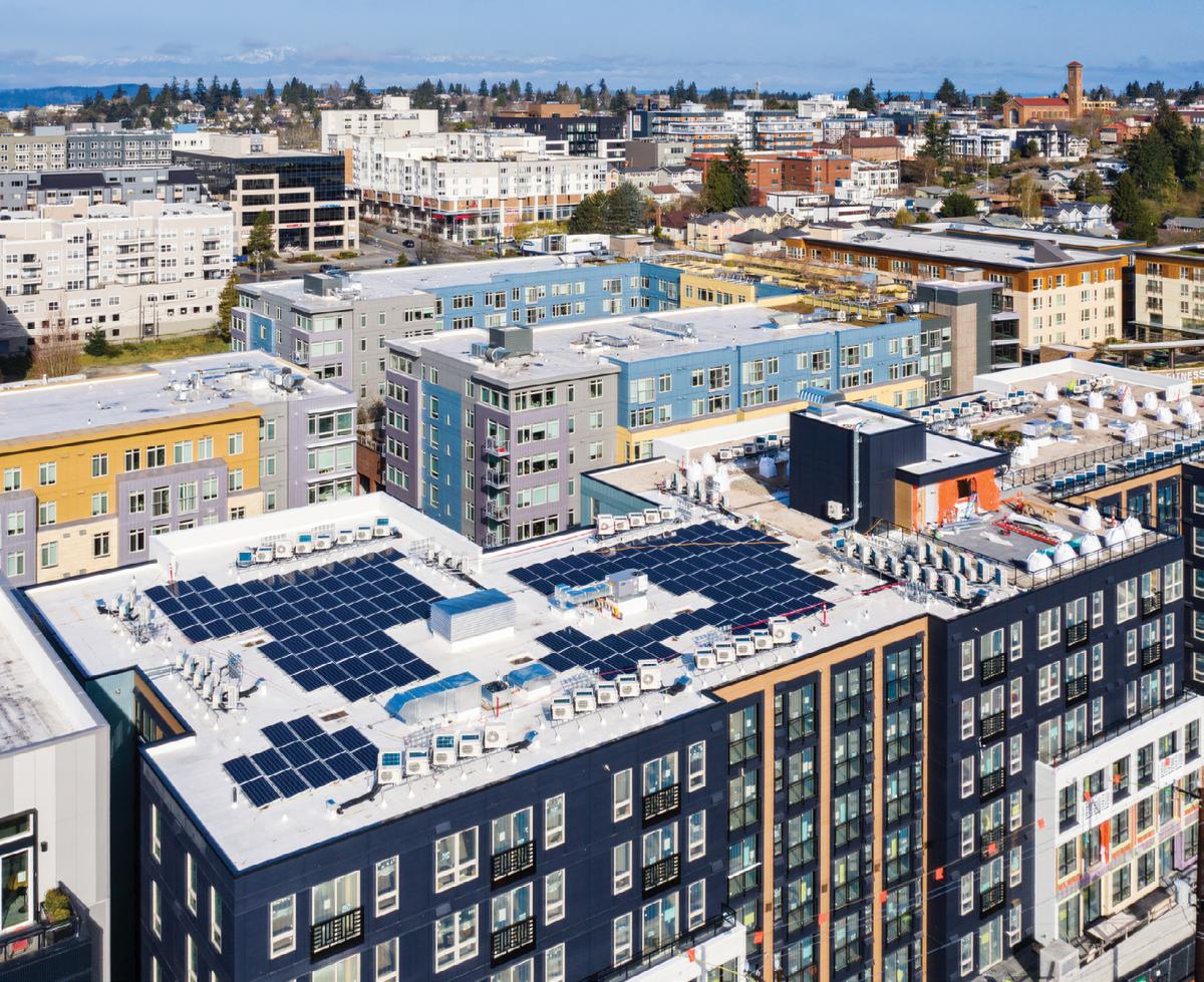 Low-angle aerial view of multistory buildings with roof-top solar panels on the building in the foreground.