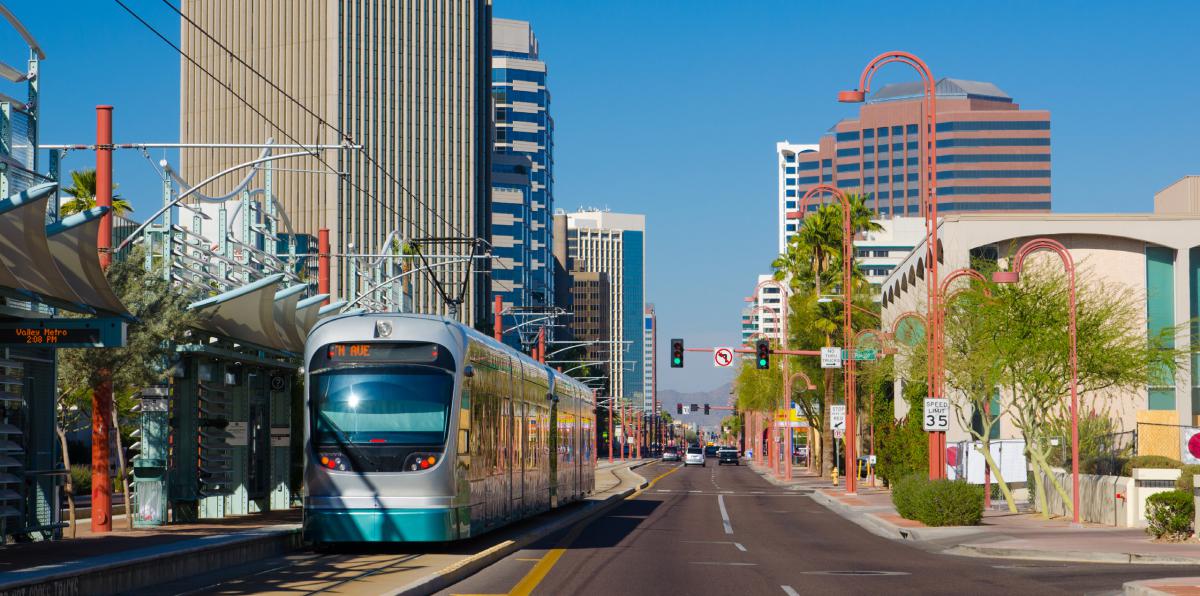 Photo of a light rail train on a street with multistory buildings.