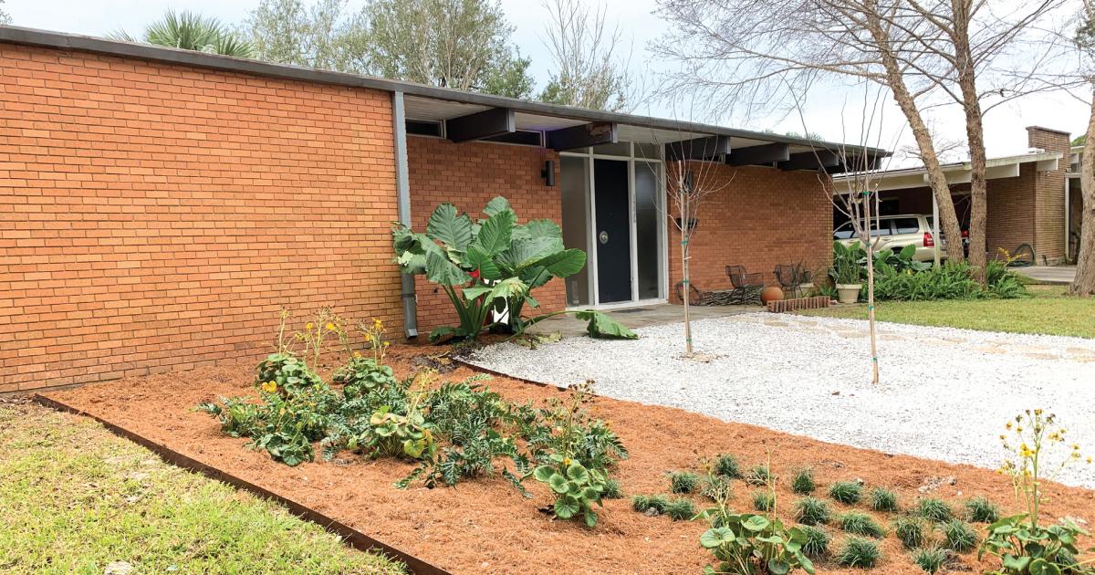 Photo of a one-story brick home and front yard with gravel, plants, and pine straw.