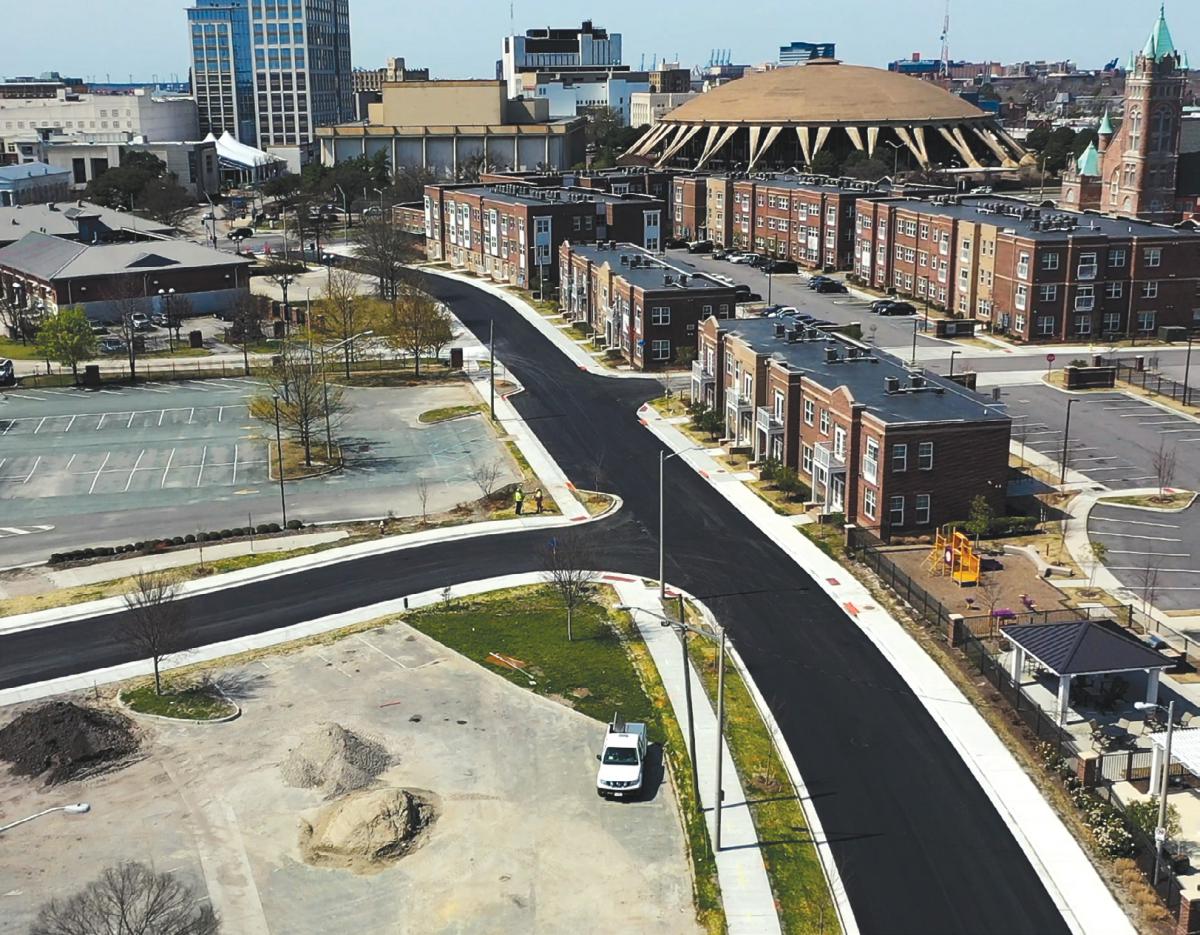 A low-angle aerial view of parking lots, roads, and several blocks of two- and three-story buildings.