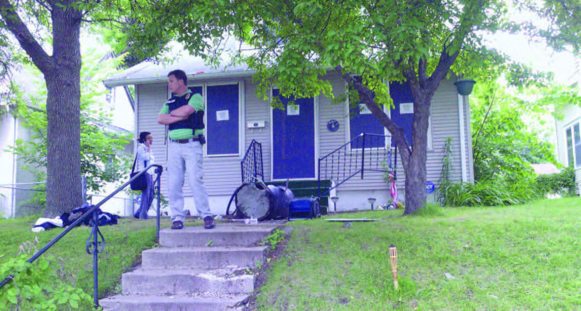  Front view of a single-family home with notices on the door and windows and two people standing in the front yard with steps in the foreground.