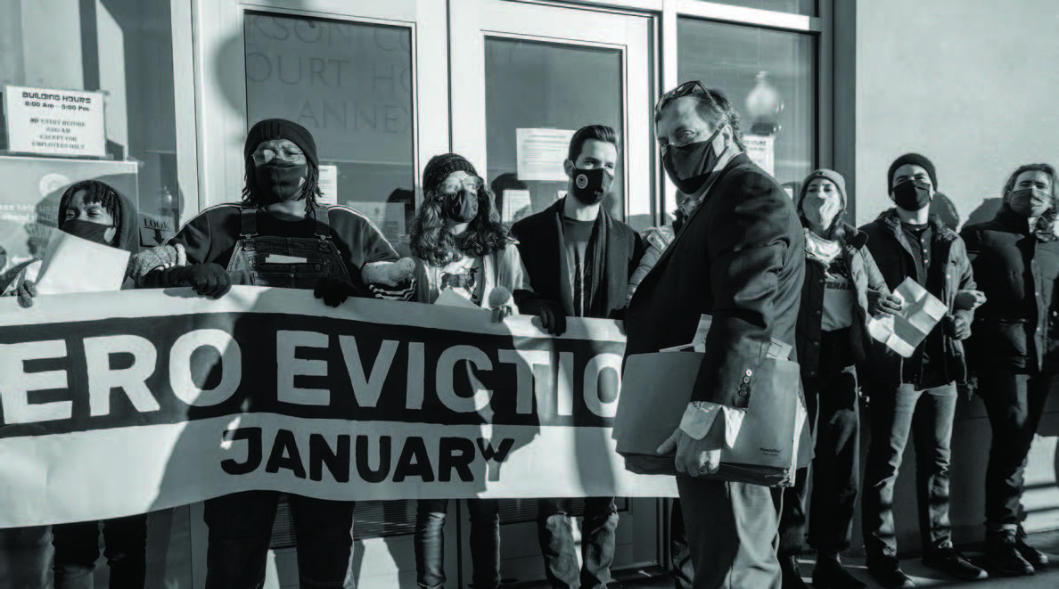  People standing outside in front of closed glass doors of a building holding a banner and blocking access to a person standing in front of them.