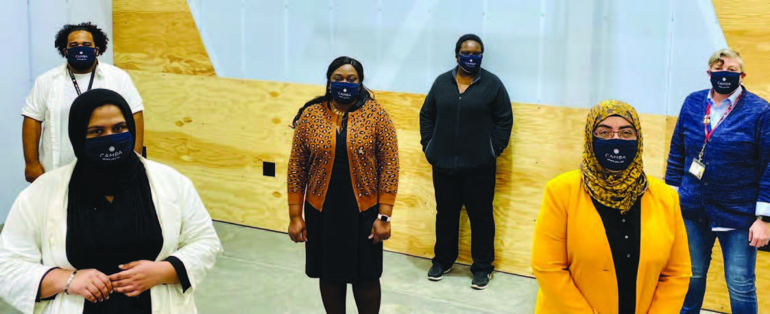  Six people standing in a group two feet apart from each other wearing face masks saying “CAMBA”.