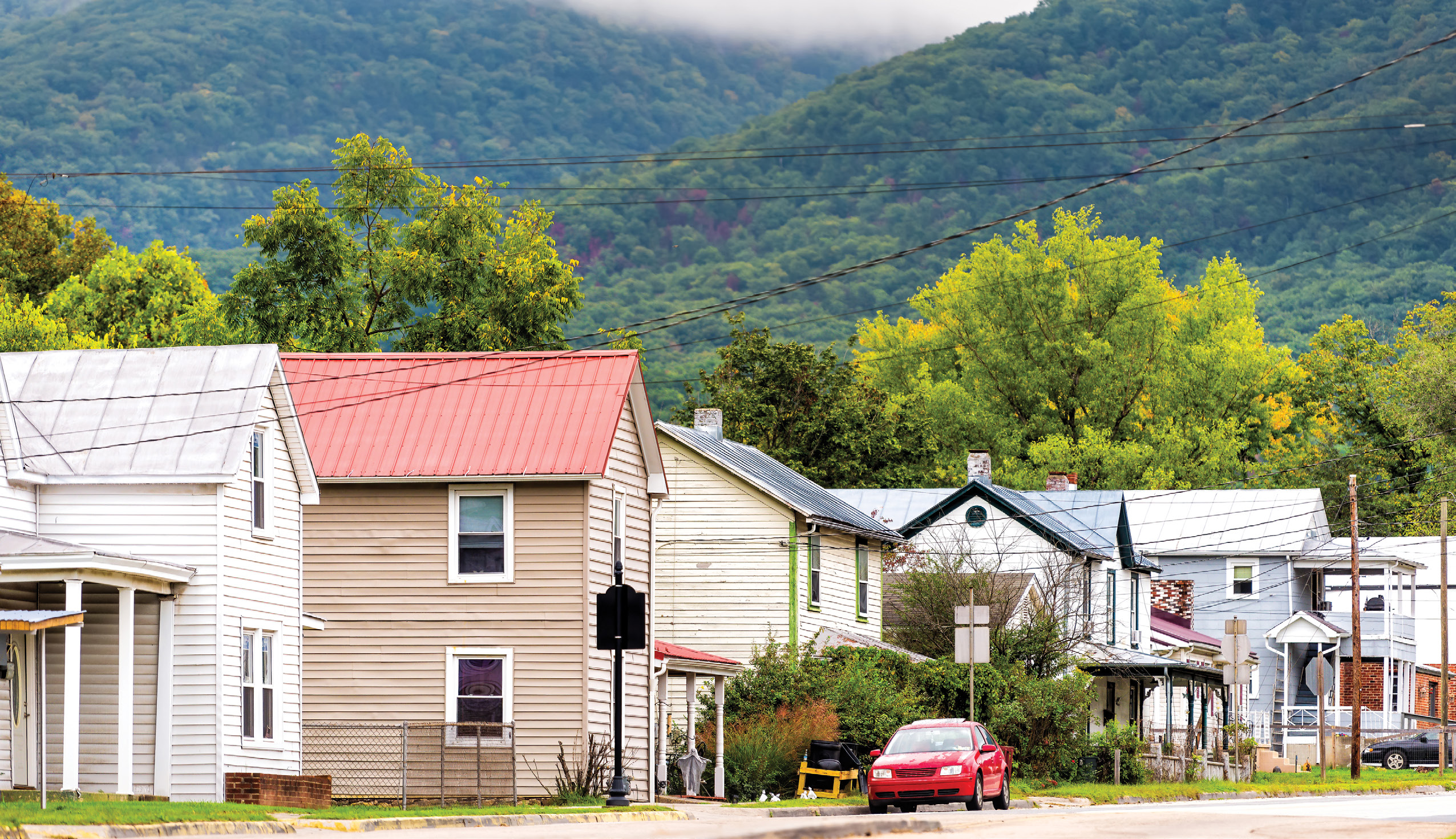 A row of small homes along a street with green, tree-covered mountains in the background.