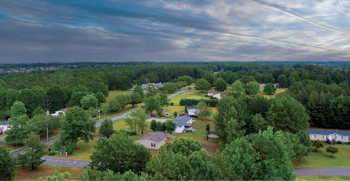 Aerial view of scattered houses surrounded by dense greenery and woods.