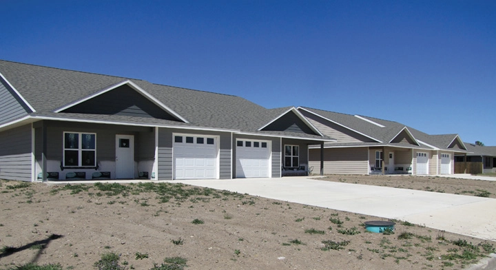 A row of new single-story houses with attached garages and concrete driveways under a clear blue sky.