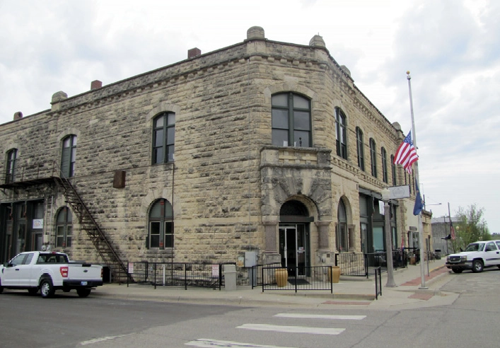 A historical two-story stone building with arched windows and a fire escape on one side on a street corner.