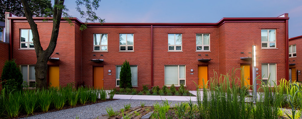 Photograph of the front façades of four townhouses in a flat-roofed, two-story brick building.