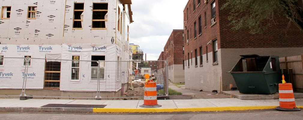 Photograph of two adjacent three-story residential buildings. On the left is a wood-frame building under construction, and on the right is an old brick building.