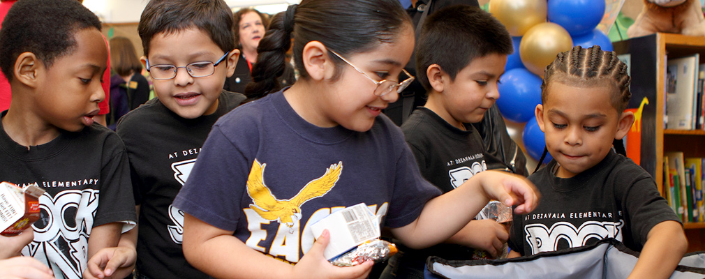 Photograph of five children inside a classroom selecting breakfast items from insulated containers.