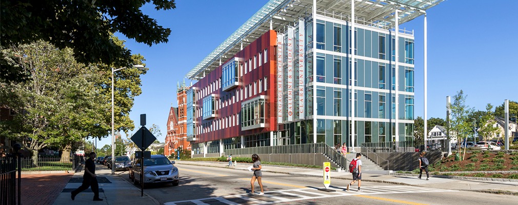 Photograph of the front and side façades of a five-story office building with a glass front and a flat roof with wide overhangs.