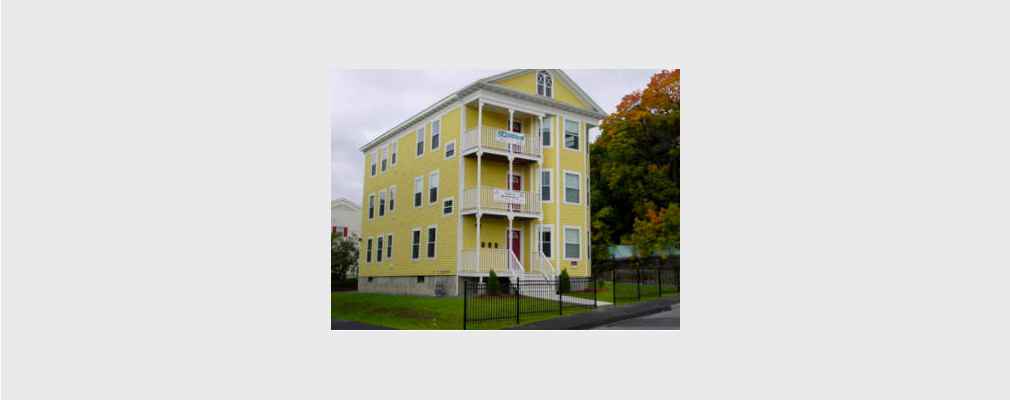 Photograph of a three-story residential building made with wood siding and having a porch on each floor.