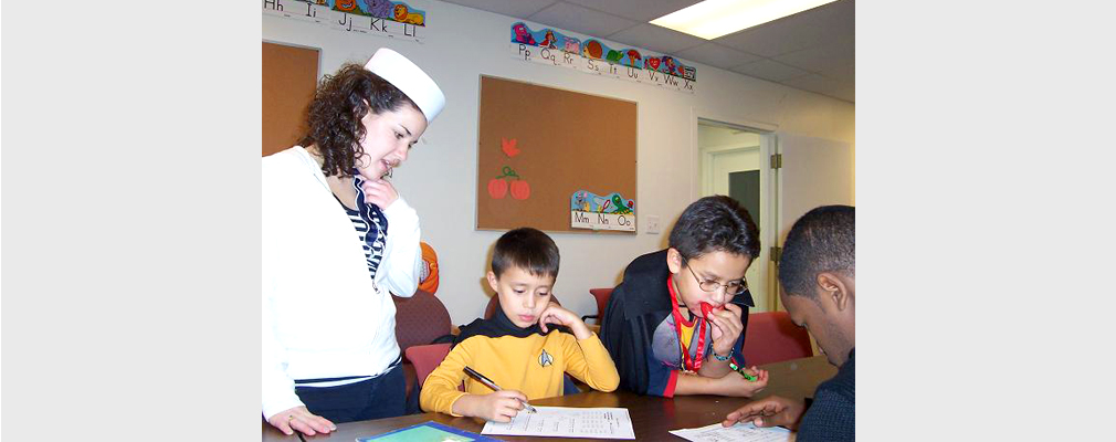 Photograph of two Clark University students and two youths in Halloween costumes working at a table.