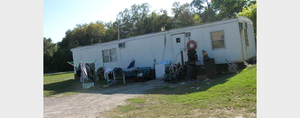 Photograph of the front of a manufactured house in poor repair.