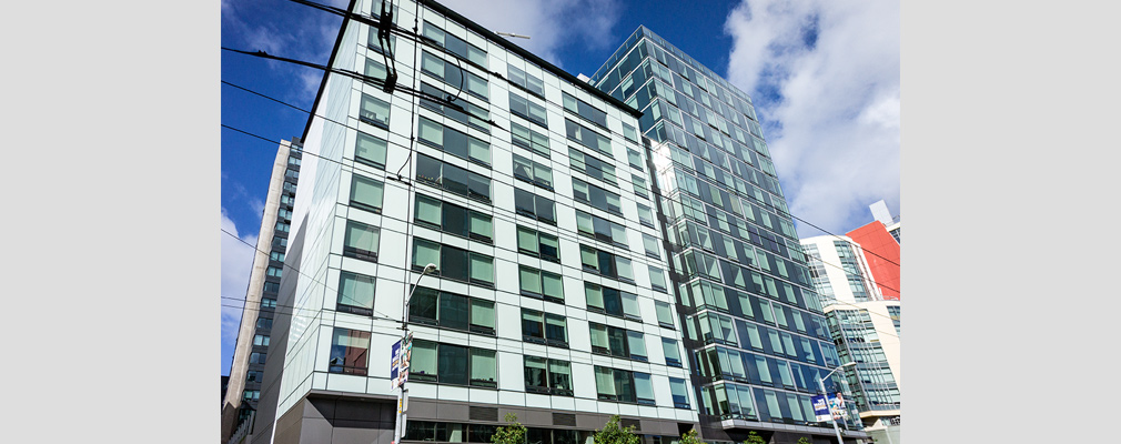 Photograph of the front façade of an apartment building with a 15-story section and a 10-story section.