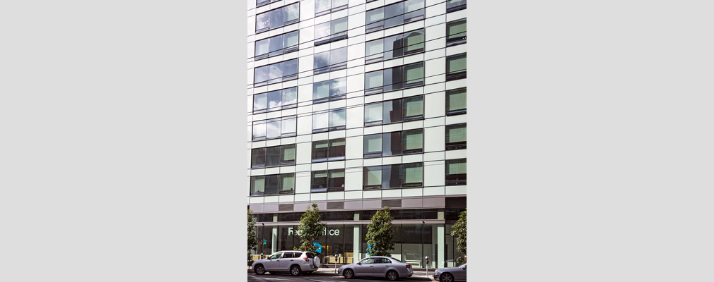 Photograph of the front façade of a high-rise residential building with shops on the ground floor.