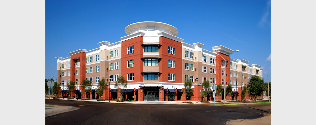 Photograph of the front façade of a four-story building containing residences above commercial spaces on the ground floor.