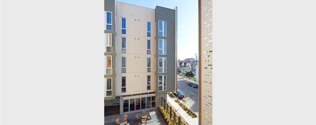 A top-down view of a courtyard with tables and chairs between two masses of a five-story apartment building.