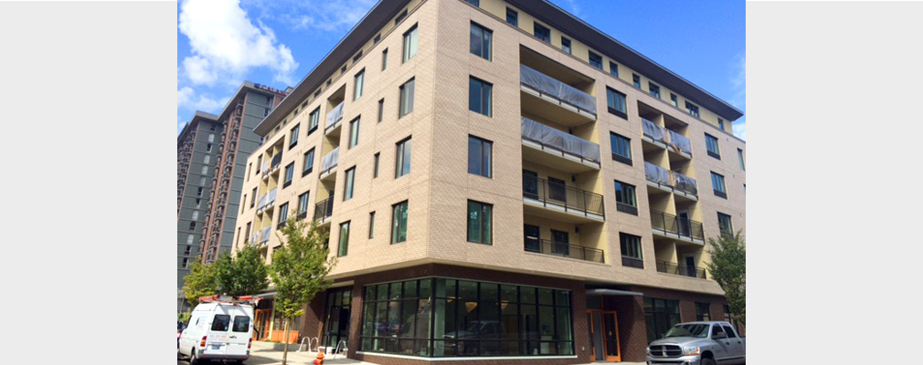 Photograph of the front and side façades of a six-story building with commercial spaces on the ground floor and apartments on the upper floors.