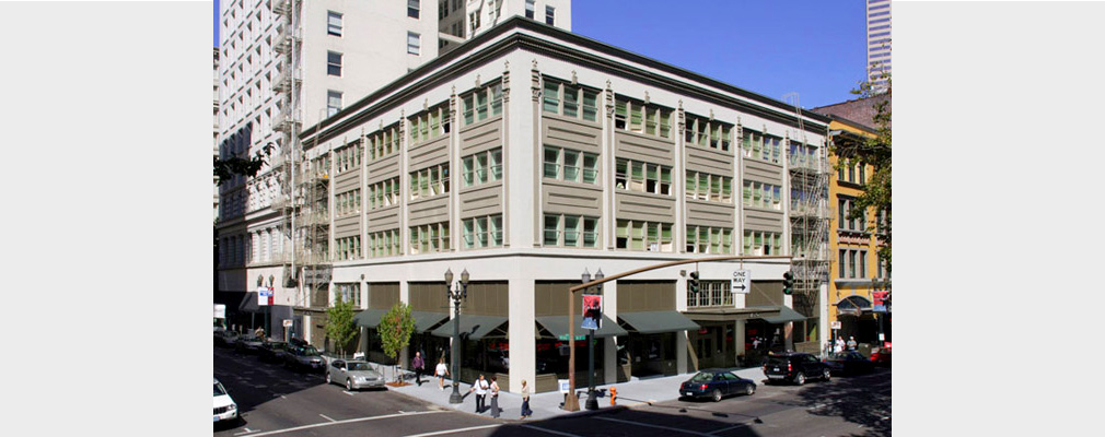 Photograph of the front and side façades of a four-story masonry building with commercial spaces on the ground floor and residences on the upper floors.