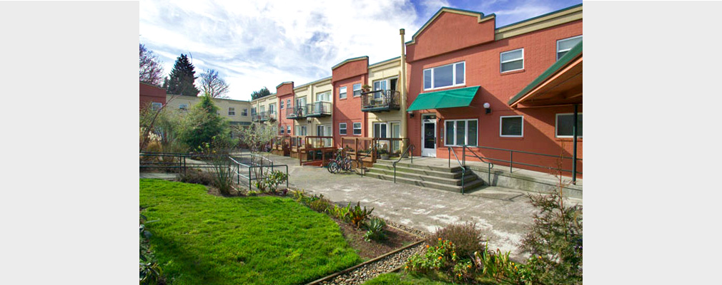 Photograph of the front façade of a two-story apartment building with communal greenspace in the foreground.