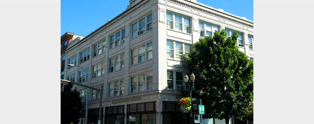 Photograph of the front and side façades of a four-story building with commercial space on the first floor and residences on the upper floors.