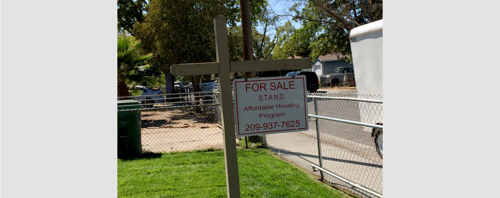 Photograph of a for-sale sign erected by STAND posted on a front lawn in a single-family neighborhood.