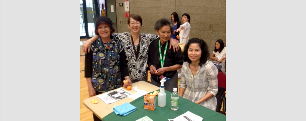 Photograph of four women at a table with informational flyers, baking soda, vinegar, a spray bottle, and a cloth.