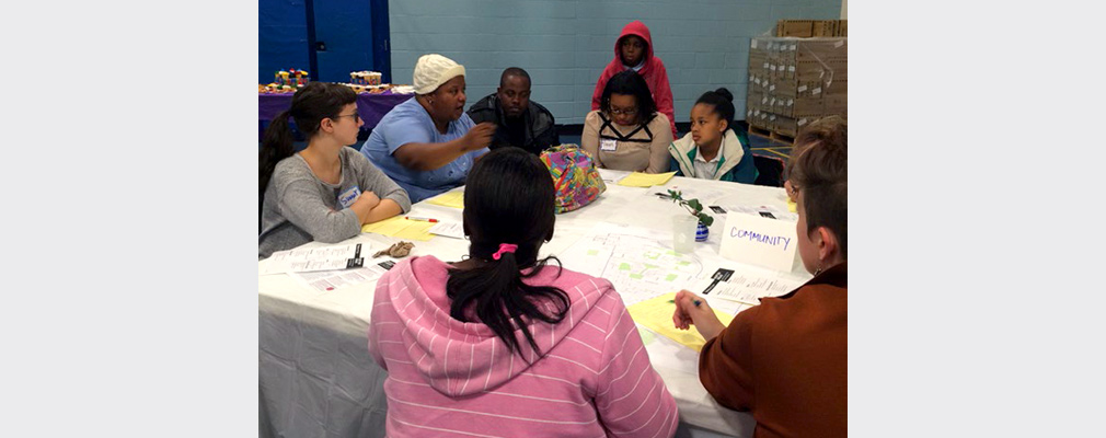 Photograph of approximately a half dozen residents participating in a discussion around a table in a large meeting room.