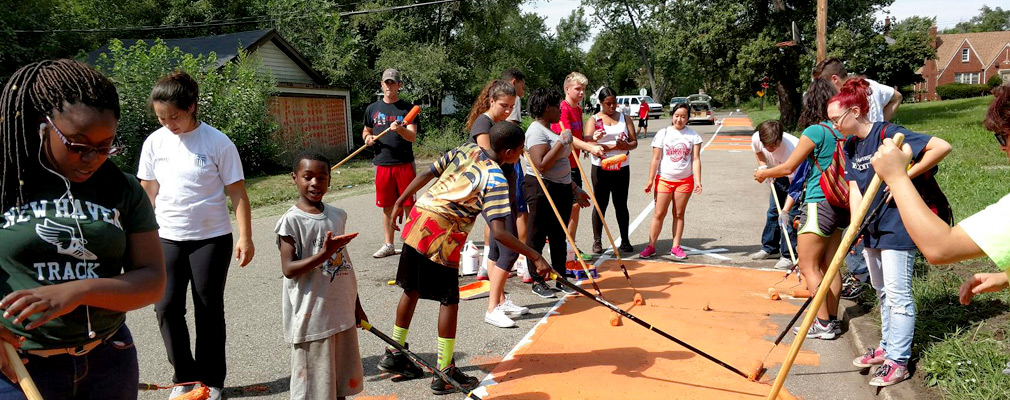 Photograph of approximately a dozen youth and adults painting a bike lane on a neighborhood street. 