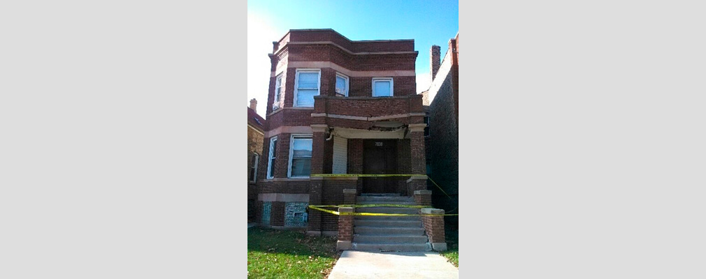 Photograph of the front façade of a two-story detached house with yellow tape cordoning off the front steps and porch. 