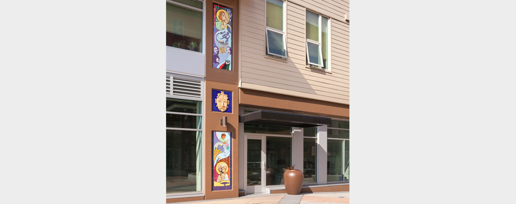 Photograph of three multicolored mosaics placed one above the other on the first and second stories of a building façade.