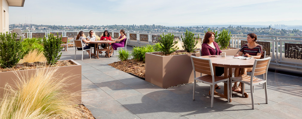 Photograph of six people seated at two circular tables on a rooftop terrace.