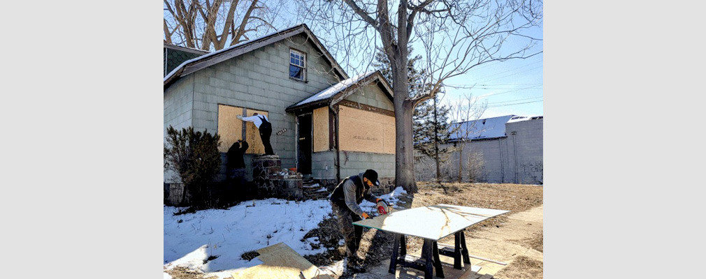 Photograph of three men boarding up the windows of a vacant house. 