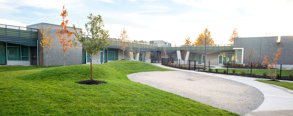 Photograph of landscaped play areas, with a one-story school building in the background.